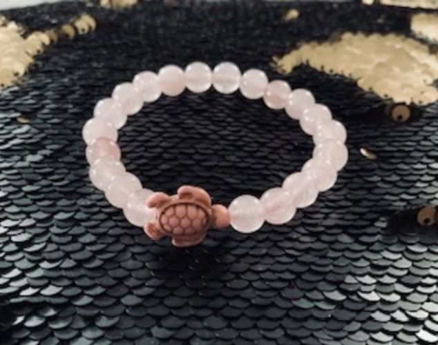 A turtle is sitting on top of a pink bracelet.