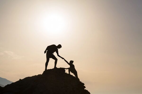 Two people on top of a hill helping each other.